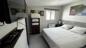 A bedroom with a bed, a TV mounted on the wall, a window, and a painting of a kayaker.