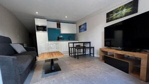 A modern living room with a sofa, coffee table, TV stand, and a kitchen area in the background.