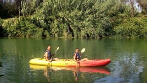 Two people kayaking on a calm river surrounded by dense greenery.