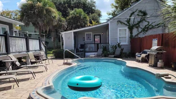 A swimming pool with a floating ring, surrounded by a tiled deck and outdoor furniture. - Relaxing Poolside Condo (Savannah)