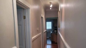A narrow hallway with wooden flooring and white walls, leading to a kitchen area. - Relaxing Poolside Condo (Savannah)