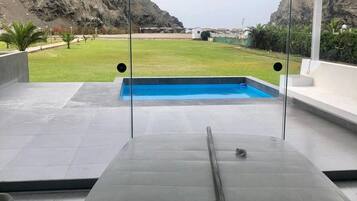A pool area with a view of a mountainous landscape, a clear sky, and a modern outdoor seating area.