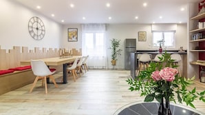 A spacious dining area with a wooden table and chairs, a clock on the wall, and a kitchen in the background.