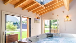 A hot tub in a room with wooden beams, large sliding glass doors, and a view of a backyard.