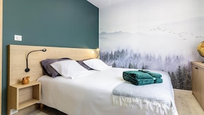 A neatly made bed with a white and gray duvet, a wooden headboard, and a small bedside table with a lamp and a decorative item.
