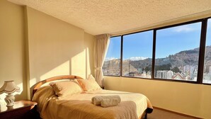 A bedroom with a large bed, a nightstand, a lamp, and a view of a cityscape through a large window. - Central Apartment with Stunning Views in La Paz (La Paz)