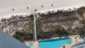 A pool area with multiple swimming pools, a staircase leading to a higher level, and a view of a beach with people in the distance. - Cozy beachside condo, great location, and fantastic views/sunsets (Panama City Beach)