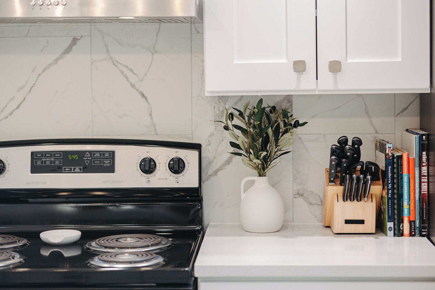 A kitchen with a stove, a white vase with green leaves, and a knife block.