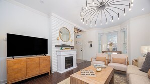 A modern living room with a flat-screen TV, wooden cabinet, fireplace, and comfortable seating. - Charming Historic Home, Luxurious Remodel, Walk to Downtown, Tree-Lined Street (Delaware)