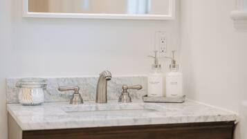 A bathroom with a marble sink, two faucets, a jar of cotton swabs, and two bottles of hand soap and lotion.