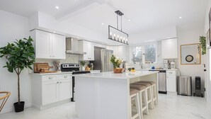 A modern kitchen with white cabinetry, a central island with stools, a stainless steel refrigerator, and a hanging light fixture. - Charming Historic Home, Luxurious Remodel, Walk to Downtown, Tree-Lined Street (Delaware)