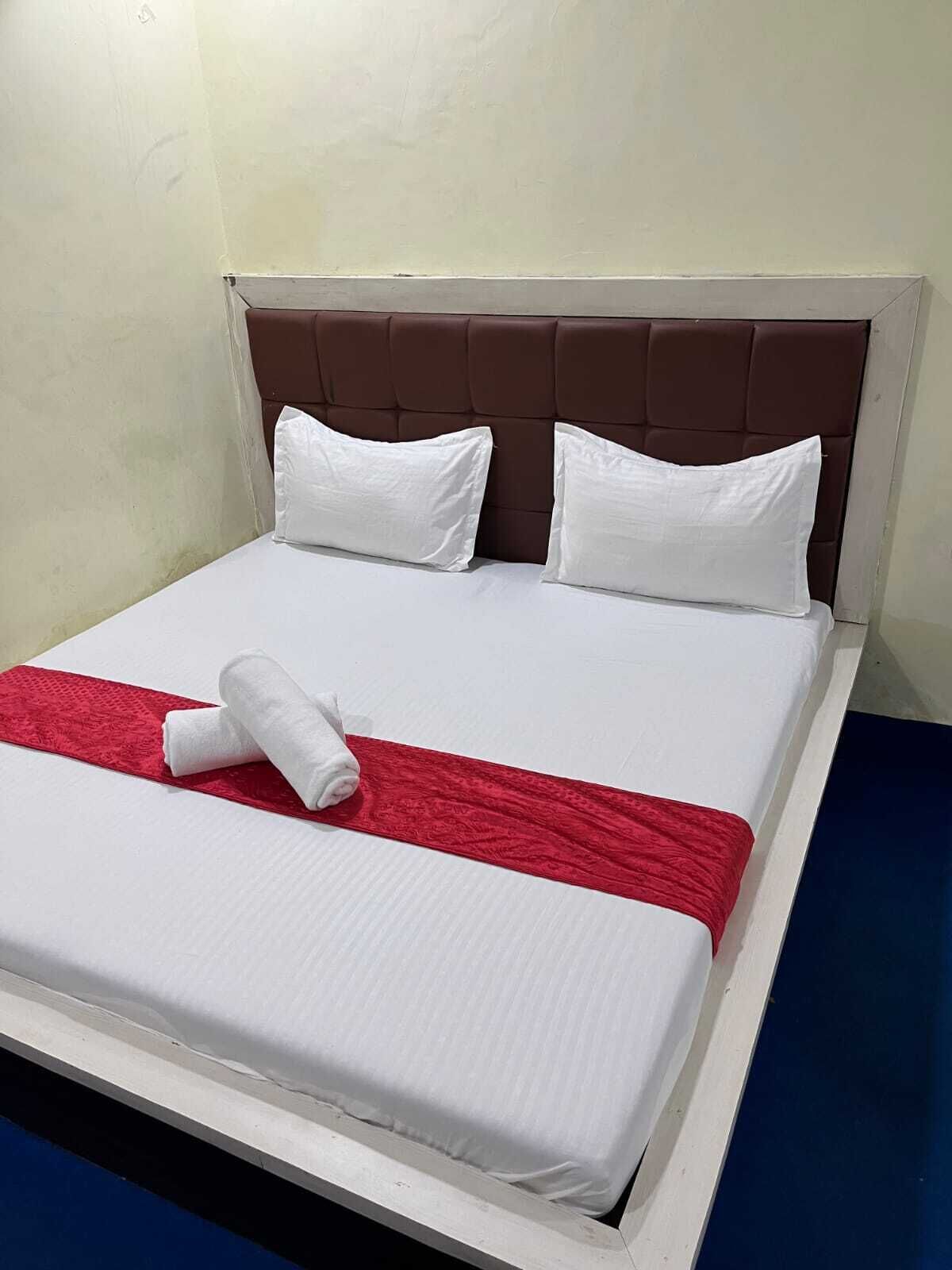 Una cama bien hecha con sábanas blancas, una manta roja y dos almohadas blancas.