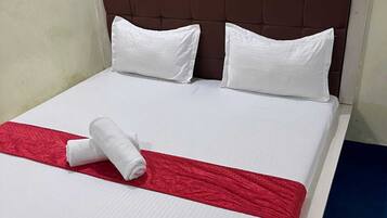 Una cama bien hecha con sábanas blancas, una manta roja y dos almohadas blancas.