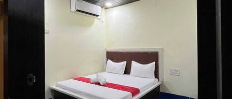 A hotel room with a bed, a ceiling fan, and an air conditioning unit.