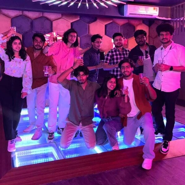 A group of people in a room with a modern design, including a hexagonal wall pattern and a floor with illuminated panels.