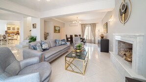 A spacious living room with a grey sofa, a glass coffee table, and a fireplace. - Irene Luxury Villa Residence | 10' drive to Lassi & Argostoli (Metaxata)