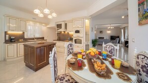A modern kitchen with white cabinetry, a central island, and a dining area with a round table set for breakfast. - Irene Luxury Villa Residence | 10' drive to Lassi & Argostoli (Metaxata)