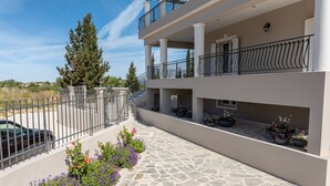 A multi-story building with a stone-paved walkway, balconies with metal railings, and potted plants. - Irene Luxury Villa Residence | 10' drive to Lassi & Argostoli (Metaxata)