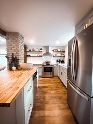 A modern kitchen with a brick accent wall, stainless steel appliances, and wooden countertops.