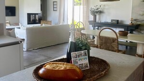 Un salon avec un canapé, une table à manger et un coin cuisine où se trouvent une bouteille de vin et un pain sur le comptoir.