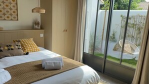 Une chambre d’hôtel avec un lit, une fenêtre donnant sur un paysage verdoyant et un fauteuil en osier à l’extérieur.