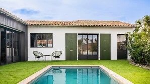 Une maison moderne avec une piscine, deux chaises et une petite table dans le jardin.