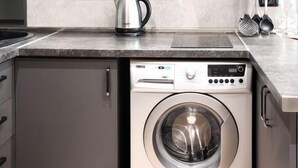 Eine moderne Küche mit grauen Schränken, einer integrierten Waschmaschine und einem Wasserkocher auf der Arbeitsplatte.