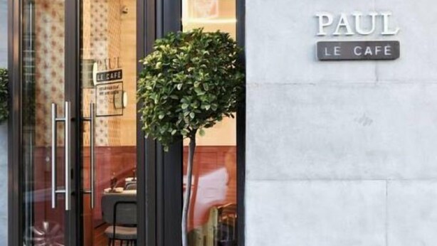 Der Eingang eines Cafés mit Glastür, einem Blumentopf und einem Schild, auf dem 'PAUL LE CAFE' steht.