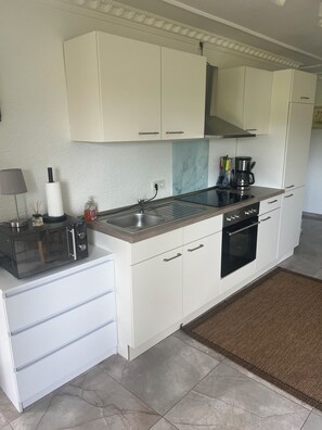 A modern kitchen with white cabinetry, a built-in oven, a coffee maker, and a microwave.