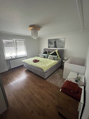 A bedroom with a bed, a bedside table, a window with blinds, and a radiator.