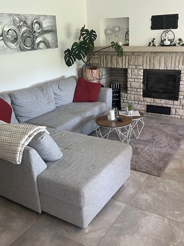A living room with a grey sectional sofa, a red throw pillow, a coffee table, a fireplace, and a large plant.