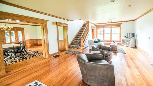 A spacious living room with hardwood floors, a staircase, a dining area with a table and chairs, and a television on a cabinet.