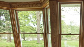 A corner room with large windows, a brick floor, and a wooden ceiling.