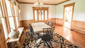 A dining room with a wooden table, chairs, a chandelier, and a patterned rug.