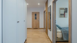 Un couloir avec un plancher en bois menant à une porte, un lit recouvert d’une couverture bleue et un miroir accroché au mur.