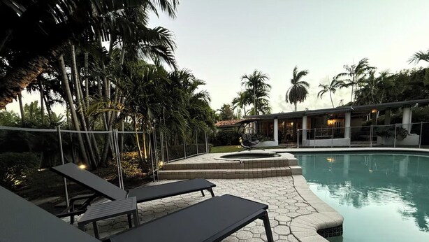 A poolside area with hexagonal tiles, lounge chairs, and palm trees.