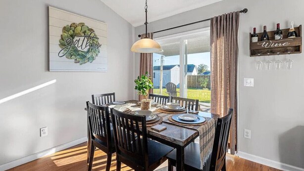 A dining area with a wooden table, chairs, and a hanging pendant light. - 4 Bed Beach Getaway! Fenced Yard + Garage Parking (Wilmington)