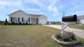 A single-story house with a front garage, a mailbox, and a well-maintained lawn. - 4 Bed Beach Getaway! Fenced Yard + Garage Parking (Wilmington)