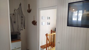 Un pasillo con escalera de madera, microondas y refrigerador.