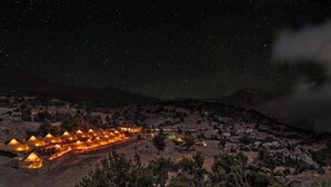 Filas de carpas iluminadas en una zona montañosa de noche.