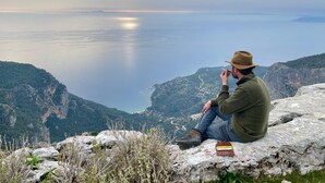 Una persona sentada sobre un saliente rocoso, con vista a un cuerpo de agua y montañas.