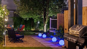 Un patio trasero con una parrilla, mobiliario exterior e iluminación decorativa.