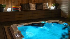 Un jacuzzi con un banco de madera y cojines, rodeado de plantas en macetas.