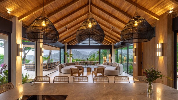 Amplia sala de estar con techos altos, ventanas grandes y vistas al exterior. Cuenta con varias zonas de estar y una mesa central.