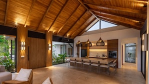 Una cocina amplia con techos altos y vigas de madera, un comedor con sillas y una mesa, y vistas a zonas verdes.