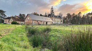 A large, historic building with multiple windows and a prominent chimney, surrounded by a grassy field and trees. - Les Longères de Montfranc (Pierrefitte-sur-Sauldre)