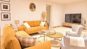 A living room with a sofa, armchairs, a glass coffee table, a TV, and framed pictures on the wall. - Les Longères de Montfranc (Pierrefitte-sur-Sauldre)