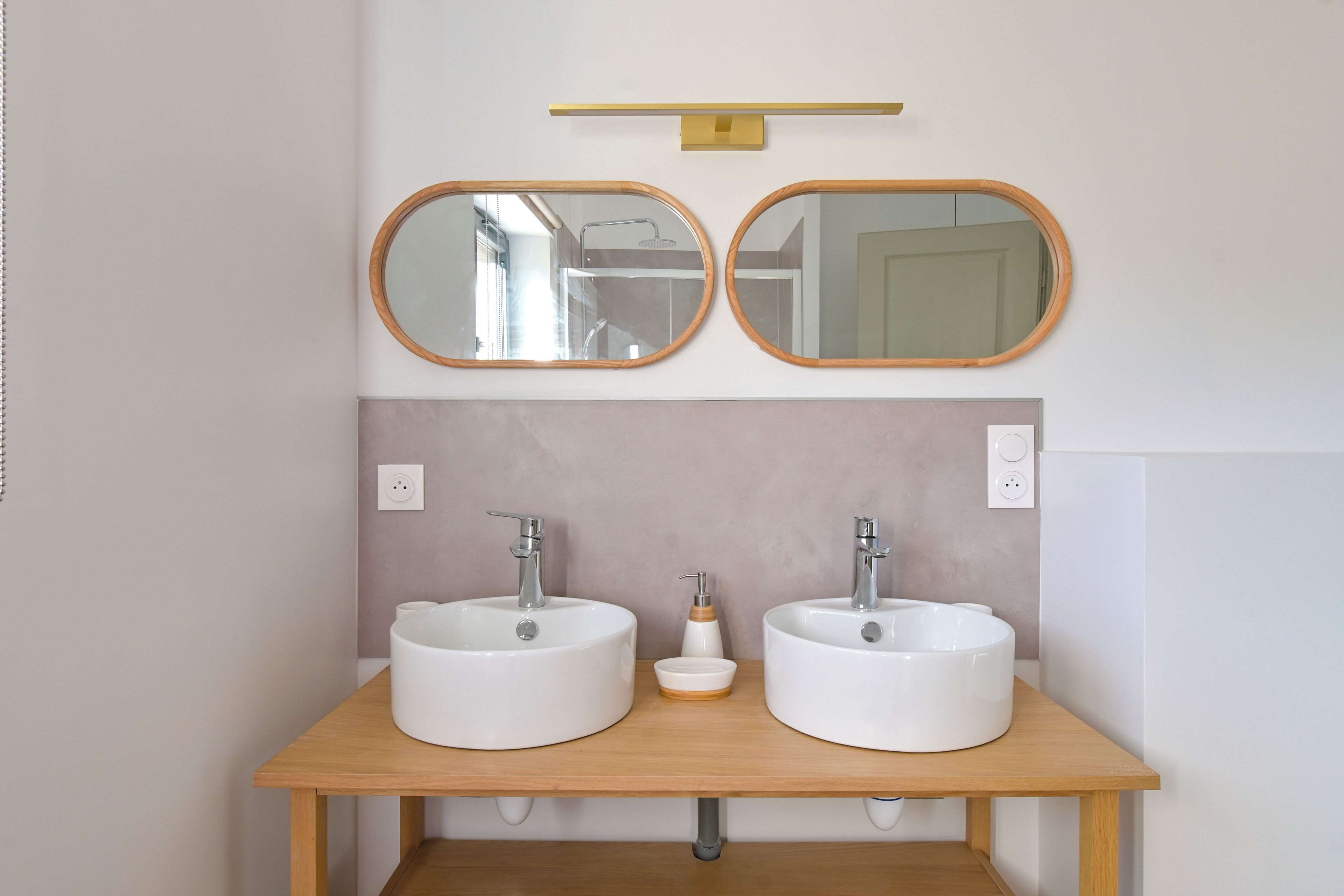 Un baño con dos lavamanos blancos, un mueble de tocador de madera y dos espejos redondos colgados en la pared.