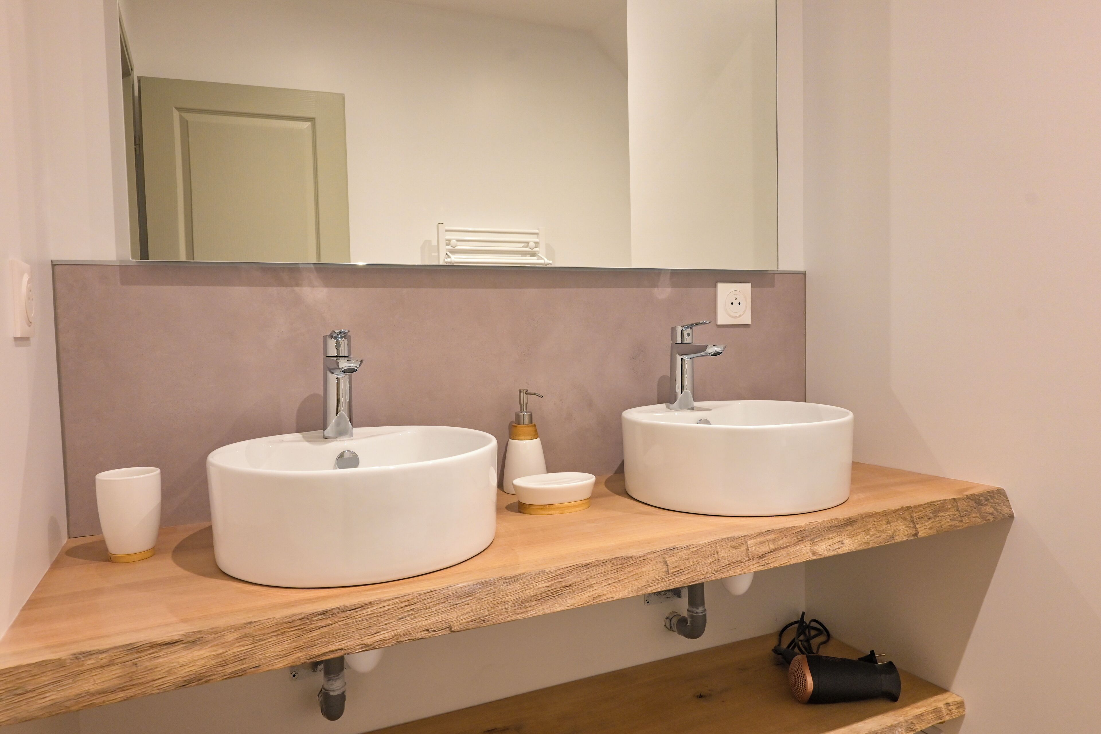 A bathroom with two sinks, a mirror, and a wooden shelf.