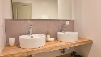 A bathroom with two sinks, a mirror, and a wooden shelf.